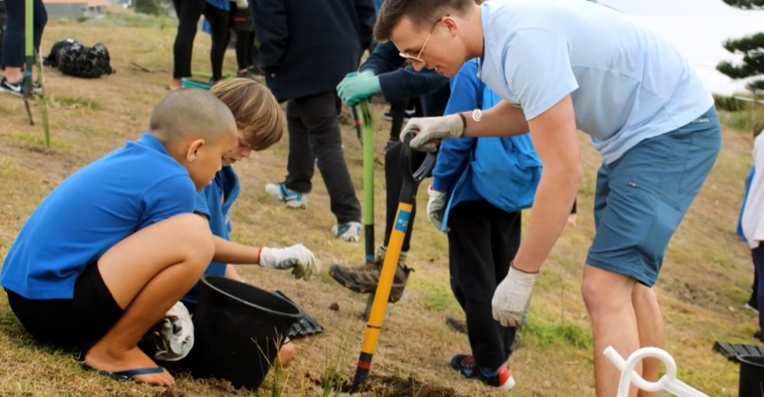 Photo of VT students helping local students from Arataki Primary School plant dune grasses