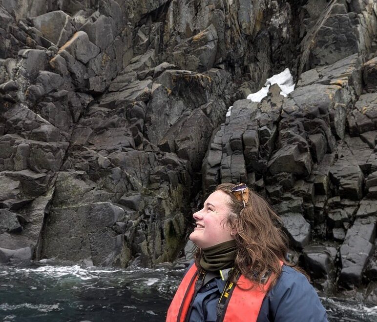 Student, Kennedy Fast, on one of the Zodiac day excursions with rocky cliff face behind