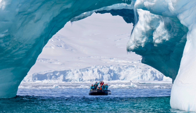 People on Zodiac boat under grand turquoise blue ice arch