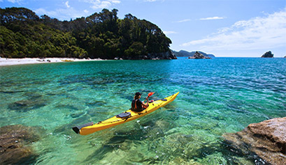 Student in yellow kayak atop the clear turquoise waters of Abel Tasman